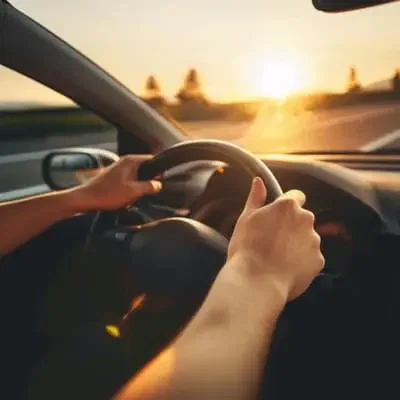 Hände am Lenkrad in einem Auto bei untergehender Sonne